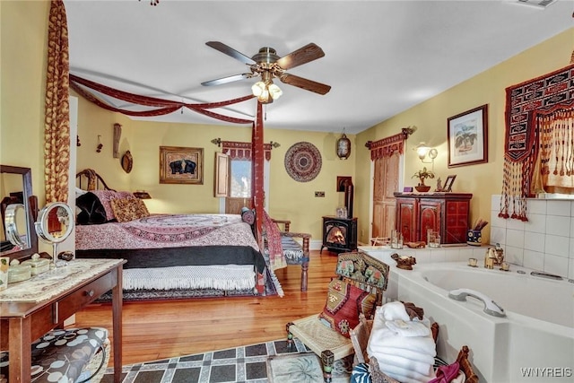 bedroom featuring ceiling fan, a wood stove, and hardwood / wood-style floors