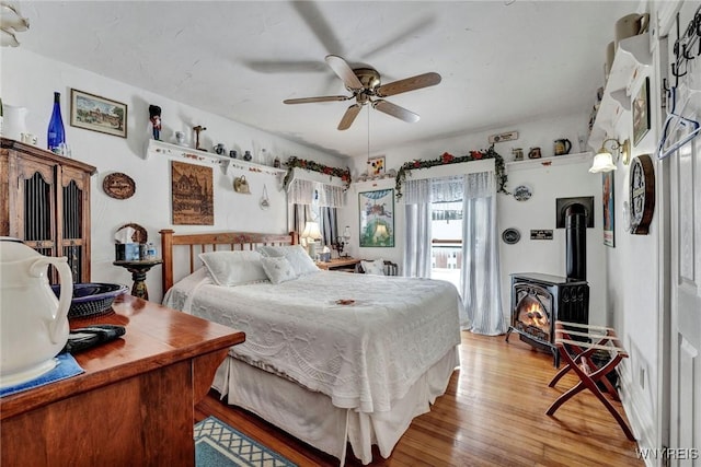 bedroom with light wood-type flooring, ceiling fan, and a wood stove