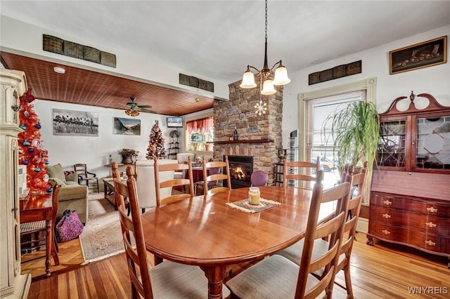 dining space featuring ceiling fan with notable chandelier, light hardwood / wood-style floors, and a stone fireplace