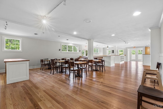 dining area featuring crown molding, light hardwood / wood-style flooring, rail lighting, french doors, and ornate columns