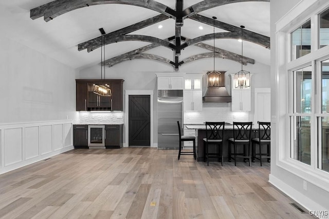 kitchen with stainless steel built in refrigerator, a notable chandelier, premium range hood, hanging light fixtures, and white cabinetry