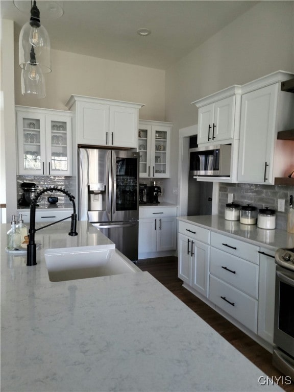 kitchen with pendant lighting, backsplash, appliances with stainless steel finishes, sink, and white cabinetry