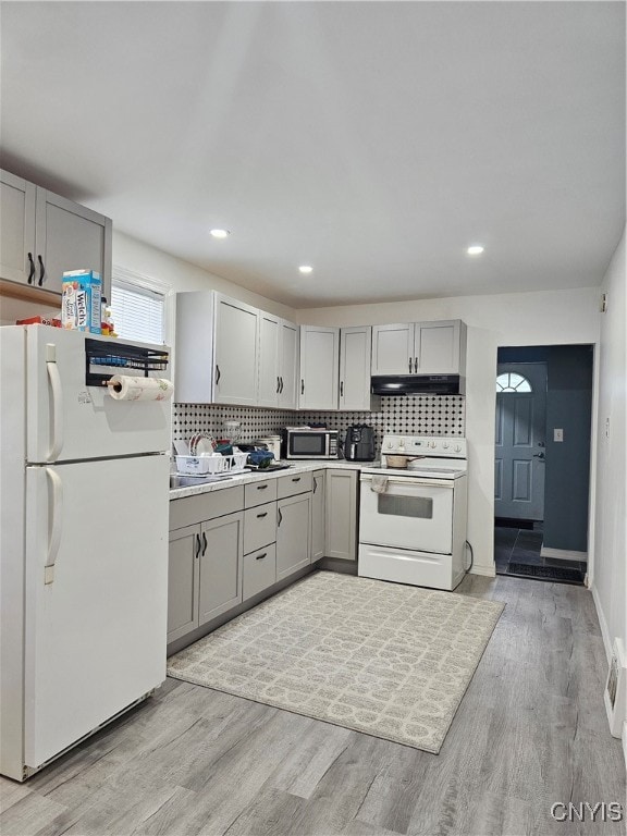 kitchen featuring light wood-type flooring, gray cabinets, white appliances, and tasteful backsplash