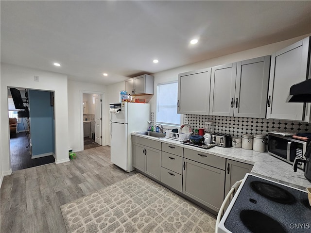 kitchen with gray cabinetry, backsplash, light wood-type flooring, white appliances, and sink