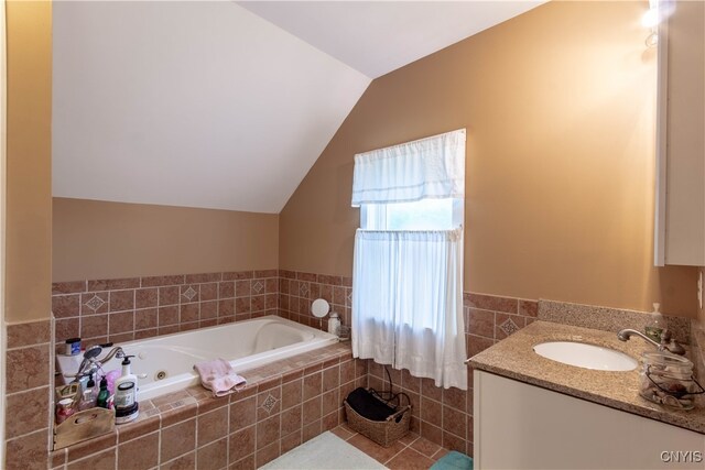 bathroom with lofted ceiling, vanity, tile patterned floors, and a relaxing tiled tub