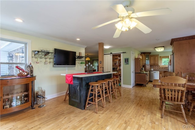 interior space featuring backsplash, ceiling fan, appliances with stainless steel finishes, a barn door, and light hardwood / wood-style floors