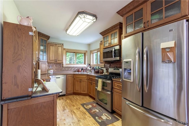318 Stevens Rd, Gouverneur, NY 13642 - kitchen with appliances with stainless steel finishes, tasteful backsplash, glass insert cabinets, light wood-type flooring, and brown cabinetry