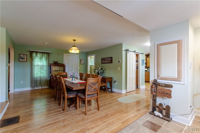 dining area with a barn door, an inviting chandelier, and light hardwood / wood-style flooring