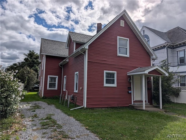 back of property featuring a shingled roof, a chimney, and a lawn