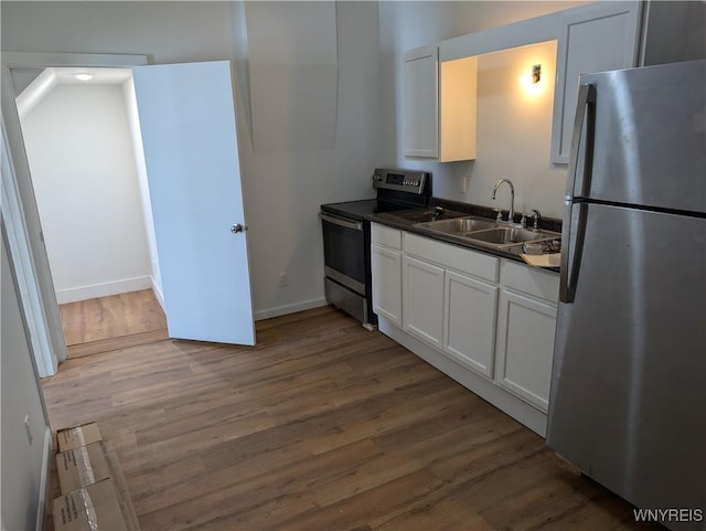 kitchen with stainless steel appliances, dark countertops, white cabinetry, a sink, and wood finished floors