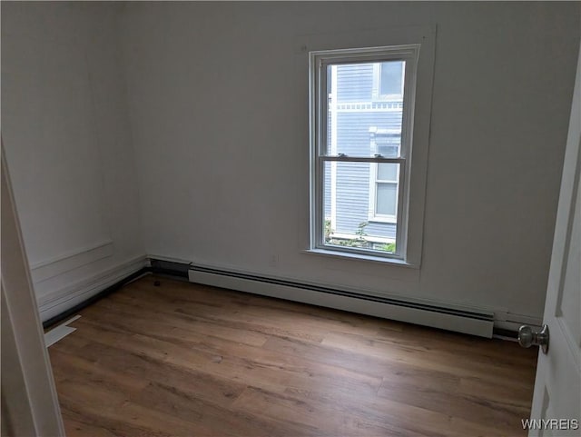 spare room with plenty of natural light, baseboard heating, and wood finished floors