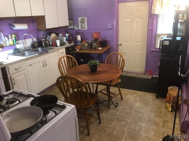 kitchen featuring white gas stove, white cabinetry, and sink