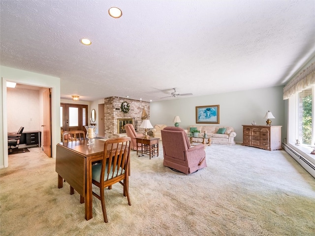 dining area featuring a fireplace, light colored carpet, baseboard heating, ceiling fan, and a textured ceiling