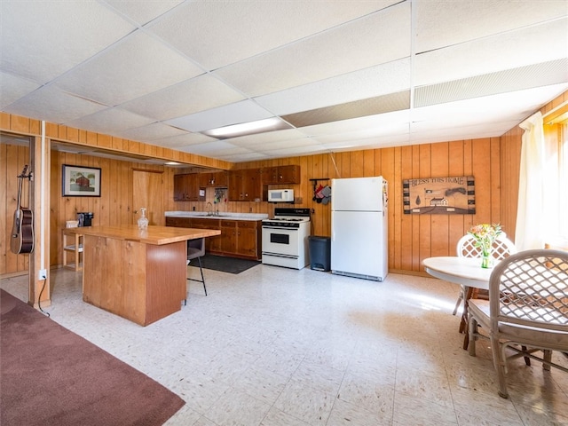 kitchen featuring wood walls, white appliances, a kitchen bar, sink, and a drop ceiling