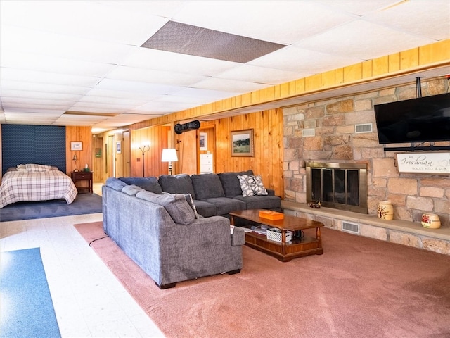 living room featuring carpet flooring, a fireplace, wooden walls, and a drop ceiling