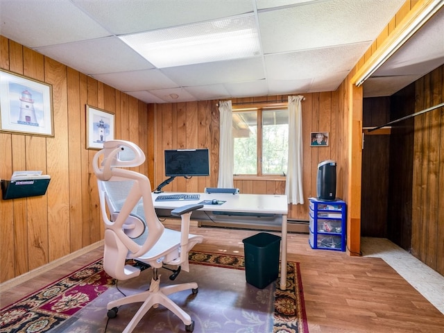 office featuring baseboard heating, wood walls, hardwood / wood-style floors, and a drop ceiling