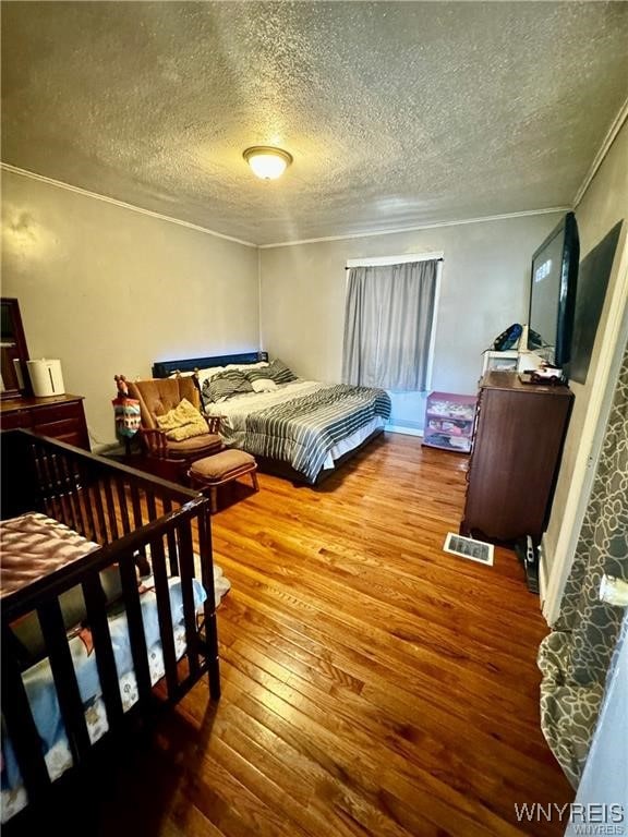 bedroom with a textured ceiling, ornamental molding, and hardwood / wood-style flooring