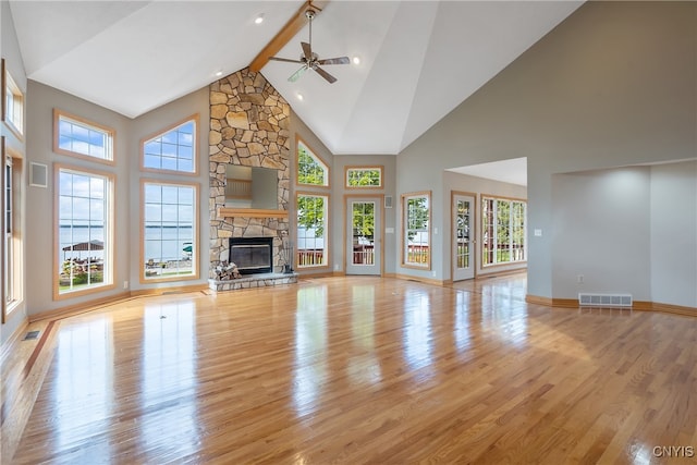 unfurnished living room featuring high vaulted ceiling, a wealth of natural light, ceiling fan, and a stone fireplace