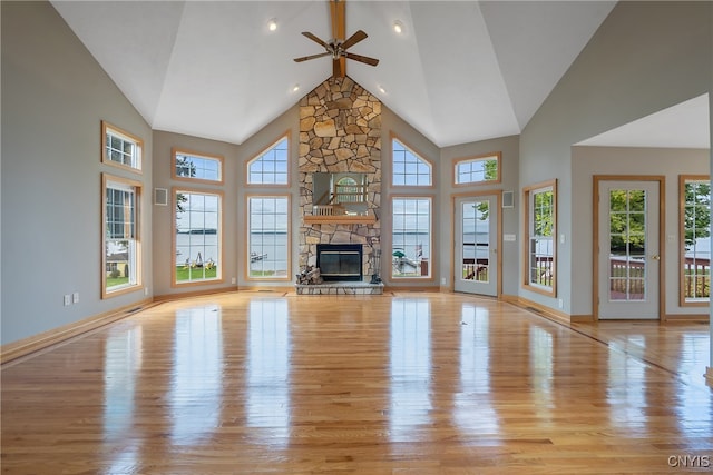 unfurnished living room featuring high vaulted ceiling, ceiling fan, light hardwood / wood-style floors, and a stone fireplace