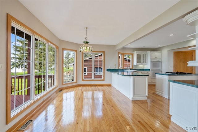 kitchen with white cabinets, light hardwood / wood-style floors, a chandelier, double oven, and pendant lighting