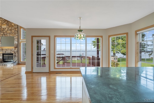 unfurnished dining area featuring light hardwood / wood-style flooring, plenty of natural light, a notable chandelier, and a stone fireplace