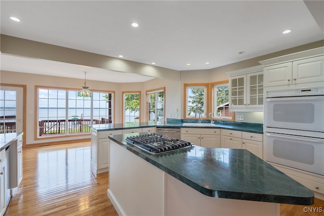 kitchen with light wood-type flooring, white cabinetry, stainless steel appliances, a kitchen island, and sink