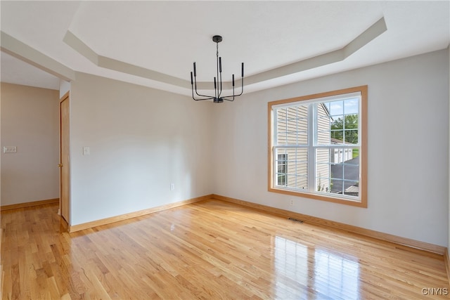 empty room featuring a raised ceiling, a chandelier, and light hardwood / wood-style flooring