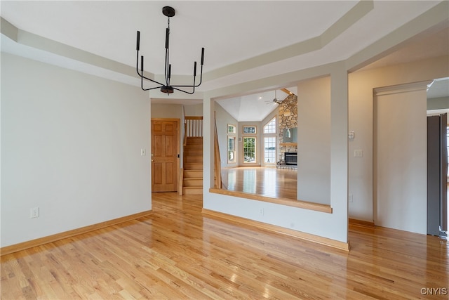 unfurnished living room with a fireplace, a chandelier, light hardwood / wood-style floors, lofted ceiling, and a raised ceiling