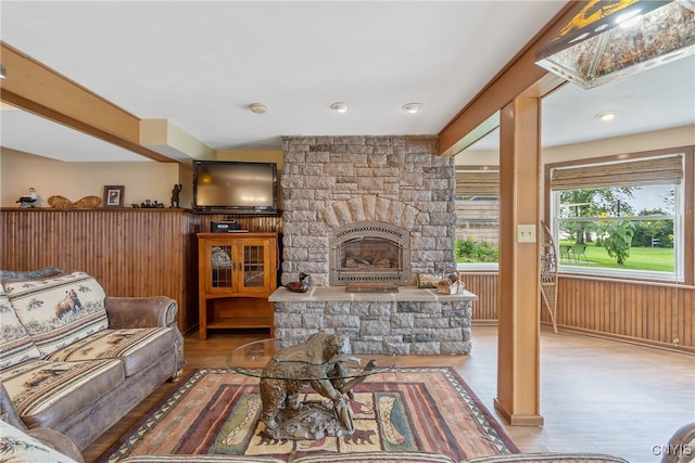 living room featuring wood-type flooring, wood walls, and a stone fireplace