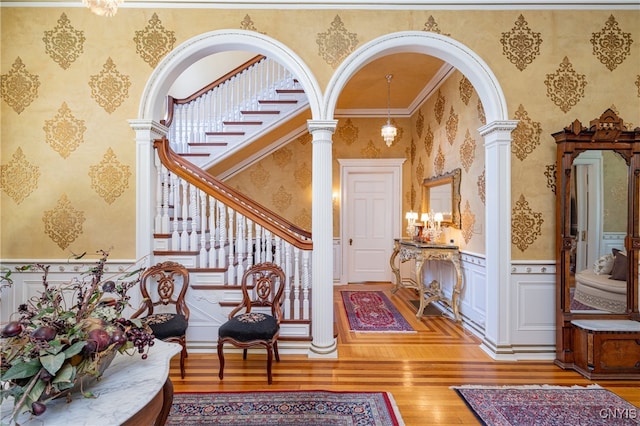 entrance foyer with ornamental molding, a chandelier, hardwood / wood-style floors, and ornate columns