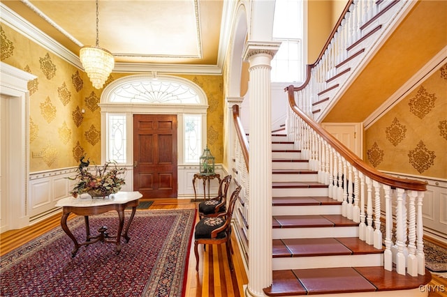 foyer entrance with a notable chandelier, wood-type flooring, decorative columns, and crown molding