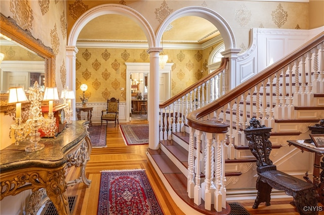 stairway featuring hardwood / wood-style flooring, crown molding, and ornate columns