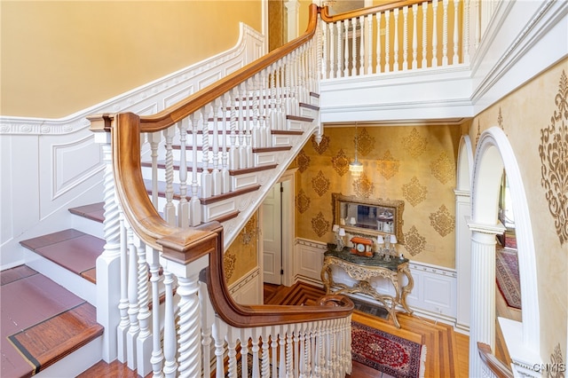 stairs featuring wood-type flooring, ornamental molding, and a towering ceiling