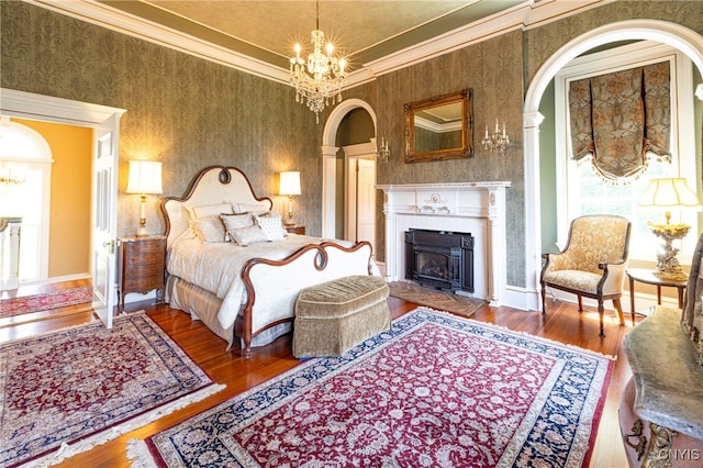 bedroom featuring a tiled fireplace, crown molding, hardwood / wood-style flooring, and a chandelier