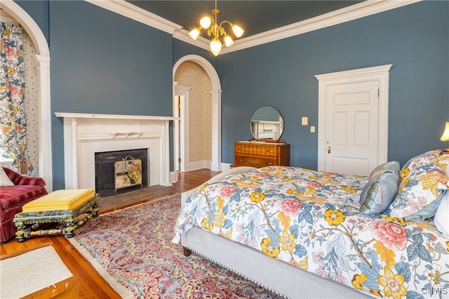 bedroom with wood-type flooring, ornamental molding, a tile fireplace, and a chandelier