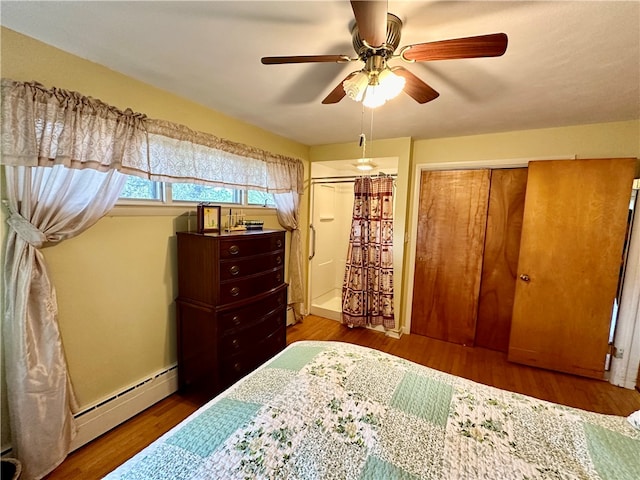 bedroom featuring baseboard heating, ceiling fan, a closet, and wood-type flooring