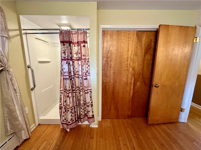 interior space with baseboard heating, a shower with curtain, and hardwood / wood-style flooring