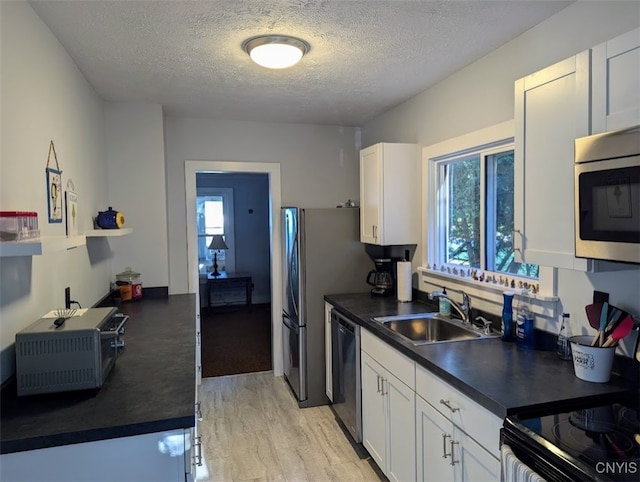 kitchen with appliances with stainless steel finishes, a textured ceiling, white cabinetry, and sink