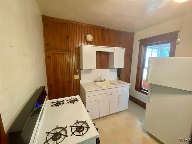 kitchen with wood walls, white refrigerator, stove, sink, and white cabinetry