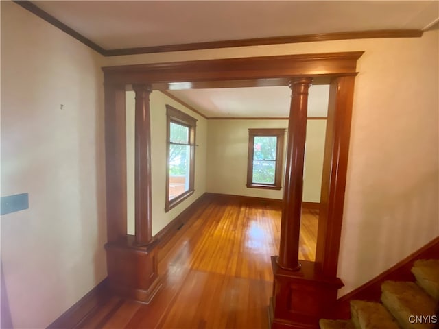 hallway featuring wood-type flooring, ornamental molding, and decorative columns