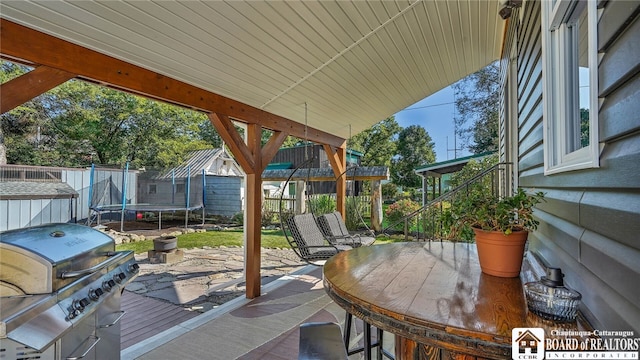 view of patio featuring a grill, a storage unit, a wooden deck, and a trampoline