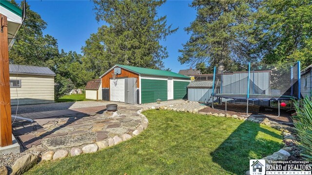 view of yard featuring a trampoline, a garage, a storage unit, and a fire pit