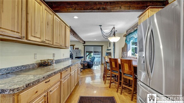 kitchen with light wood-type flooring, light brown cabinetry, hanging light fixtures, stainless steel fridge with ice dispenser, and beam ceiling