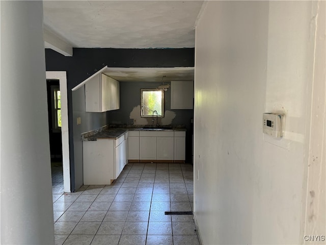 kitchen with sink, light tile patterned floors, beam ceiling, and white cabinets