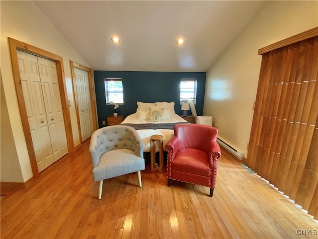 bedroom featuring a baseboard heating unit, light wood-type flooring, lofted ceiling, and two closets