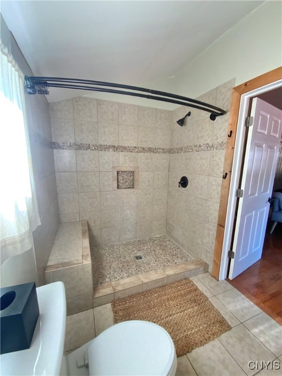 bathroom featuring wood-type flooring, toilet, and a tile shower