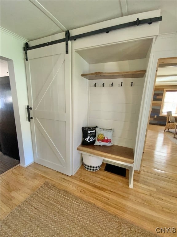 mudroom featuring a barn door, light wood-type flooring, and crown molding