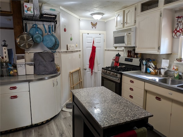 kitchen featuring light wood-type flooring, stainless steel range with gas stovetop, ornamental molding, white cabinetry, and a textured ceiling