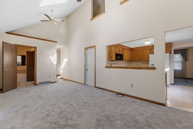 unfurnished living room with ceiling fan, light carpet, and a skylight