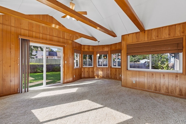 spare room featuring lofted ceiling with beams, a healthy amount of sunlight, wood walls, and carpet